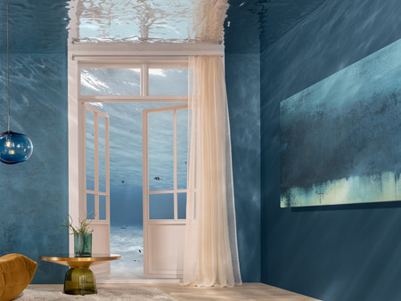 Ein stilvolles Zimmer mit blauen Wänden und natürlichem Licht. Links ein gemütlicher Sessel und Beistelltisch, rechts ein großes Farbverlauf-Bild. Große Fenster mit hellen Vorhängen sorgen für eine luftige Atmosphäre.