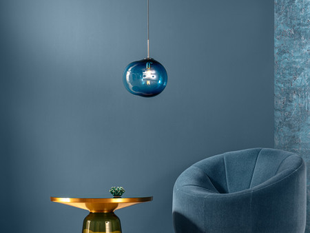 Ein stilvoll eingerichteter Raum mit einer runden blauen Couch und einem eleganten runden Tisch. Über dem Tisch hängt eine durchsichtige Lampe, die sanftes Licht ausstrahlt. Die Wände sind in dunklen Blautönen gehalten und zeigen eine sanfte Wellenbewegung, die an Wasser erinnert.